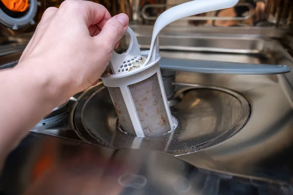 A hand taking out a dirty drain filter of dishwashing machine close up