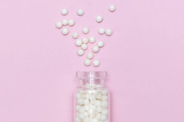 Açık pembe arka planda temiz bir cam şişeden yayılmış homeopatik küreseller, alternatif homeopati tıp konsepti