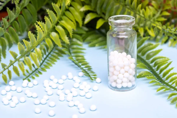 Homeopathic globules in a clear glass bottle on herbal background, alternative homeopathy medicine concept