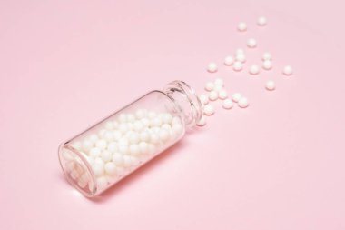 Açık pembe arka planda temiz bir cam şişeden yayılmış homeopatik küreseller, alternatif homeopati tıp konsepti