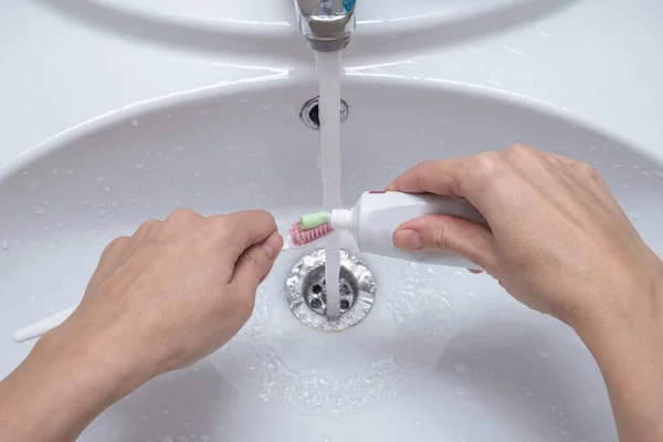 Manos femeninas poniendo pasta de dientes en el cepillo de dientes en el baño, concepto de cuidado dental y preparación para la limpieza de dientes — Foto de Stock