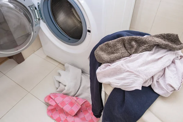Корзина для белья, полная грязного белья на полу ванной комнаты и стиральной машины, бытовая концепция — стоковое фото