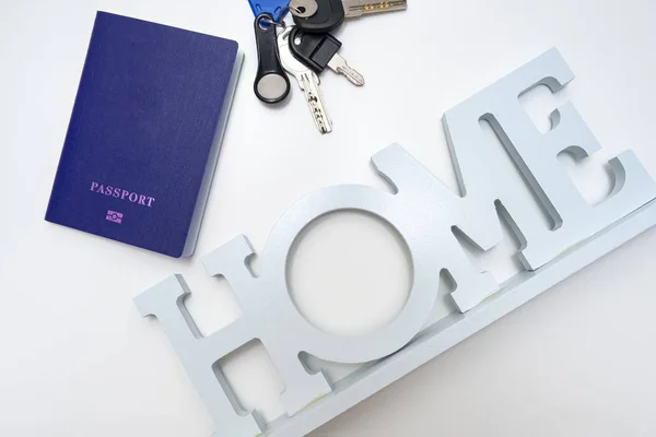 Un montón, juego de llaves de metal, pasaporte azul y un letrero casero sobre fondo blanco — Foto de Stock