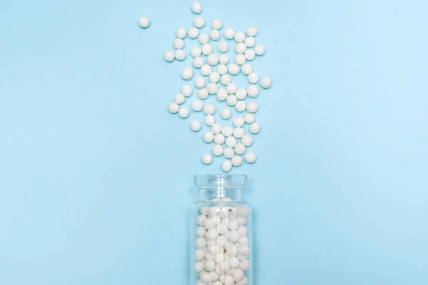 Гомеопатические глобулы, разбросанные по прозрачной стеклянной бутылке на светло-голубом фоне, альтернативная концепция гомеопатии медицины — стоковое фото