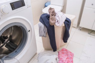 Çamaşır sepeti kirli çamaşırlarla dolu banyo zemininde çamaşır makinesi, ev konsepti..