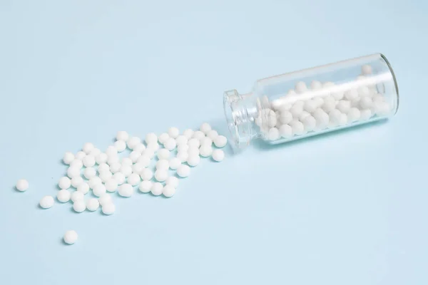Homeopatyczne Kulki Rozrzucone Przezroczystej Szklanej Butelki Jasnoniebieskim Tle Alternatywna Koncepcja — Zdjęcie stockowe