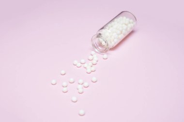 Açık pembe arka planda temiz bir cam şişeden yayılmış homeopatik küreseller, alternatif homeopati tıp konsepti.