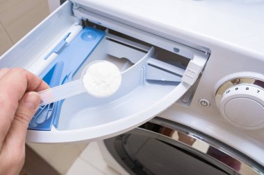Bir ev hanımı çamaşır makinesi çekmecesine fosfatsız deterjan ekliyor.