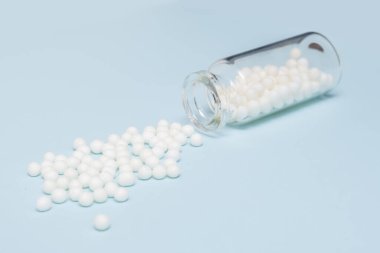 Açık mavi arka planda, temiz bir cam şişeden yayılmış homeopatik küreseller, alternatif homeopati ilacı ve naturopati konsepti.