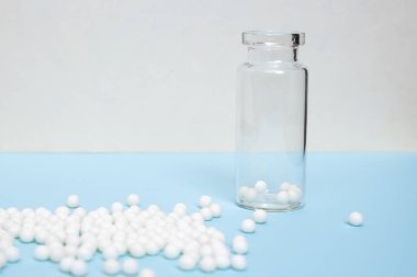 Açık mavi zemin üzerine dağılmış homeopatik küresellerle dolu temiz cam şişe, alternatif homeopati ilacı ve naturopati konsepti.