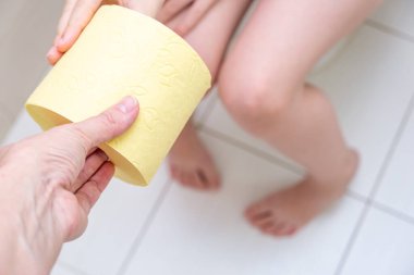 Anne oğluna bir rulo sarı tuvalet kağıdı veriyor. Tuvalette oturuyor, çocuk sindirim sorunları yaşıyor ve tuvalet kavramında zorluklar yaşıyor..