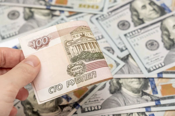 A hand holding one hundred ruble and american dollar banknotes on background, ruble devaluation and usd-rub exchange rate concept.