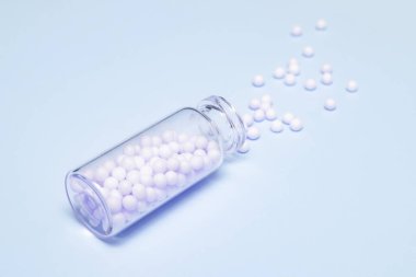 Açık mavi arka planda, temiz bir cam şişeden yayılmış homeopatik küreseller, alternatif homeopati ilacı ve naturopati konsepti.