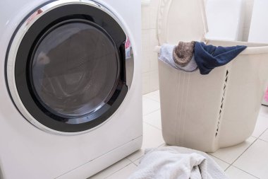 Kirli çarşaf ve kıyafetlerle dolu büyük bir çamaşır sepetinin içinde modern bir çamaşır makinesi..