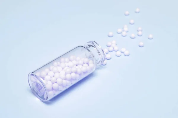 Glóbulos Homeopáticos Esparcidos Una Botella Vidrio Transparente Sobre Fondo Azul — Foto de Stock