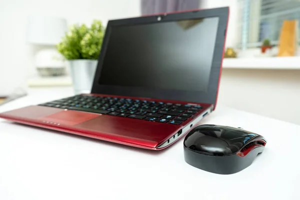 A modern red laptop and a mouse standing on white table, working space for business.