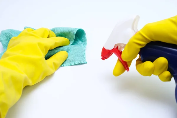 Mains en gants de caoutchouc jaune essuyant la poussière avec un chiffon en microfibre et pulvérisant avec un agent de nettoyage à partir d'un pulvérisateur, nettoyer le concept de la maison, fond blanc — Photo