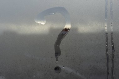 Cam, soru işareti kavramı üzerinde yazıt. Soru işareti buğulu ve ıslak pencere yüzeyinde boyanır.
