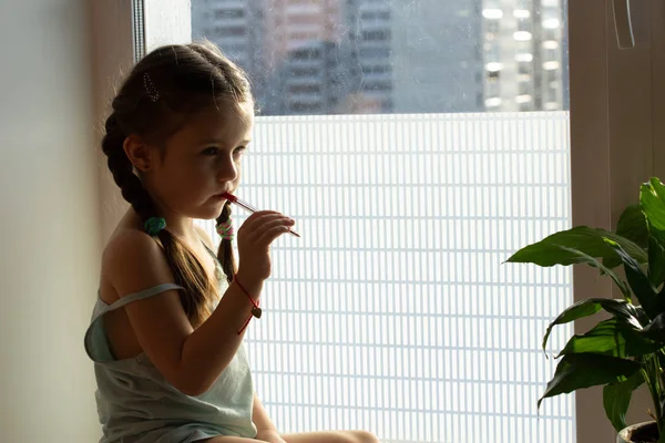Het kind zit op de vensterbank en denkt na over het album — Stockfoto