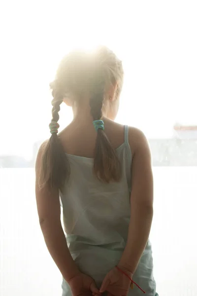 Ein Kind sitzt auf einem Fensterbrett und blickt traurig nach draußen und wartet — Stockfoto