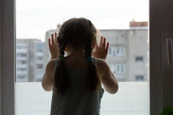 Een kind zit op een vensterbank en kijkt droevig buiten wachtend — Stockfoto