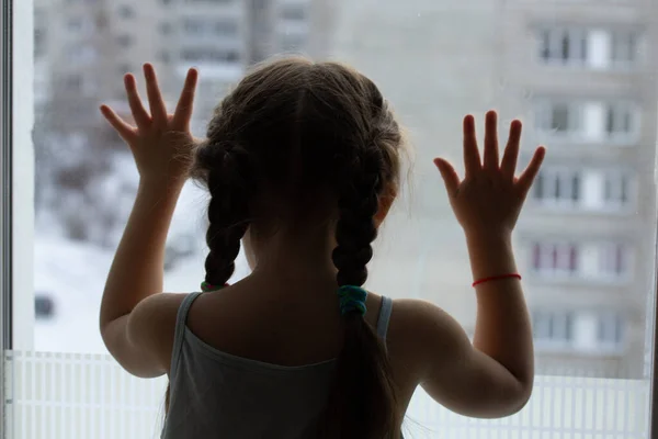 Ein Kind sitzt auf einem Fensterbrett und blickt traurig nach draußen und wartet — Stockfoto