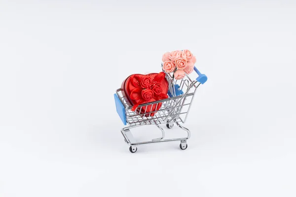 Shopping cart with presents, flowers and moneys on white background