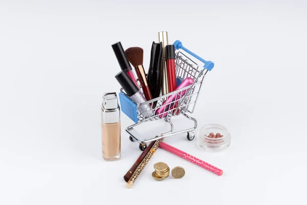 Carrinho de compras com cosméticos e dinheiro sobre fundo branco — Fotografia de Stock