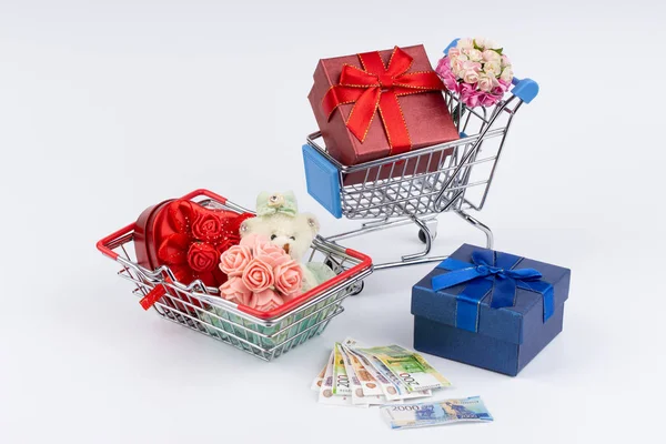 Shopping cart with presents, flowers and moneys on white background — Stockfoto