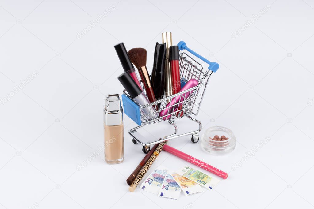Shopping cart with cosmetics and moneys on white background