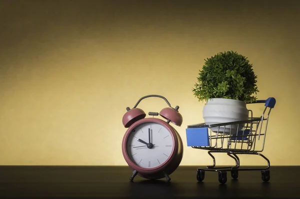 Pequeño carrito de compras y despertador sobre fondo pastel mínimo — Foto de Stock