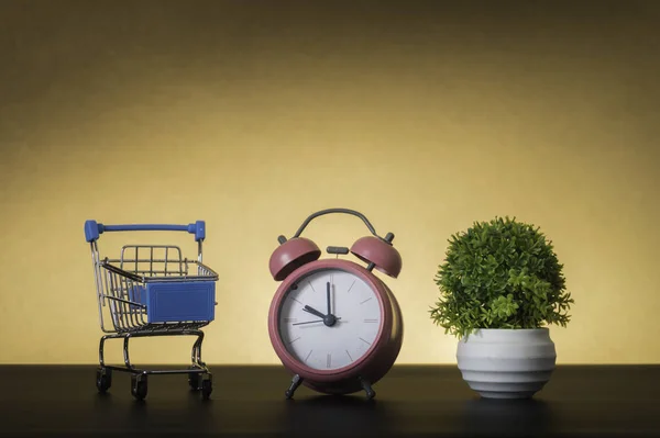 Pequeño carrito de compras y despertador sobre fondo pastel mínimo — Foto de Stock