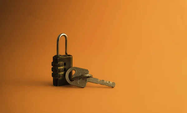 Combination padlock and key isolated on orange background.