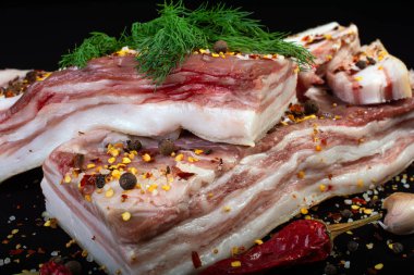 Dereotu, biber, sarımsak ve soğanla süslenmiş baharatlarla süslenmiş siyah bir zemin üzerinde et katmanları ile domuz yağı.