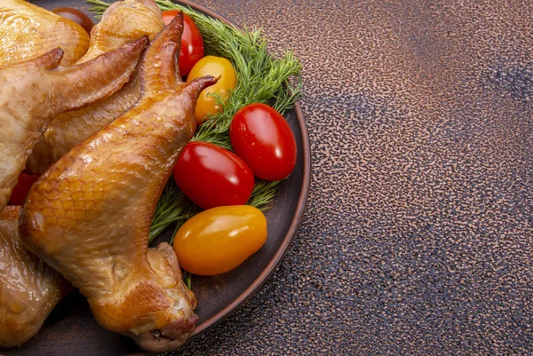 smoked chicken wings, cherry tomatoes in a plate on a textured background