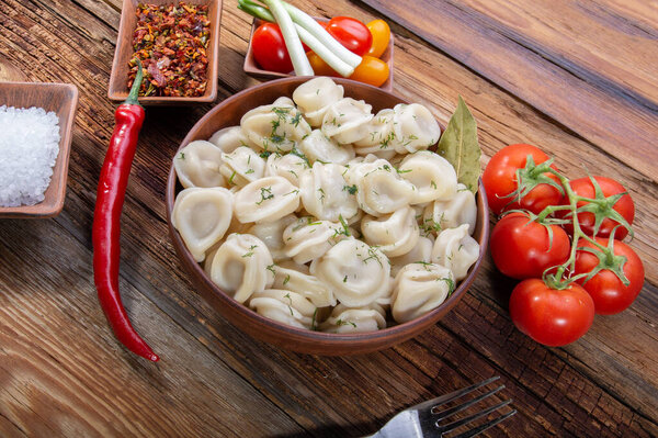 вкусные пельмени с перцем чили лук и специи в глиняной тарелке на деревянном винтажном столе вид сверху
