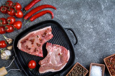 Izgara tavada iki biftek, kiraz domatesli ve koyu arkaplanda kırmızı biber.