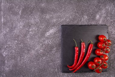 Çeri domatesleri, şist taşında kırmızı biberler, en üstte koyu dokuma arkaplanı.