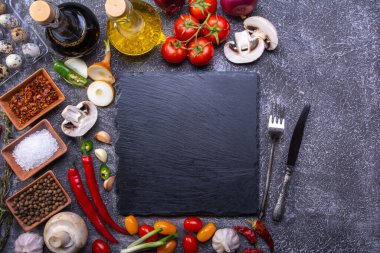 Taze sebzelerle, baharatlarla ve yemek pişirmek için malzemelerle çevrili servis taşları.