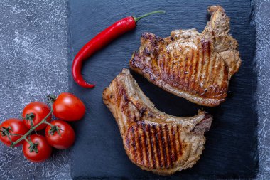 Kızarmış biftekler kiraz domatesli ve biberli yukarıdan siyah desenli arka planda.