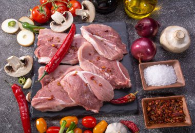 Taşta domuz bifteği, taze sebzeler, yukarıdan dokulu arka planda yakın plan pişirmek için baharatlar.