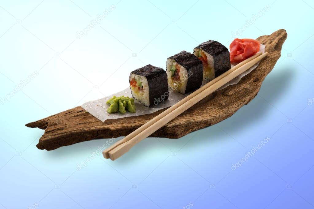 Delicious fresh sushi rolls served on a wooden rustic plate on colorful surface.