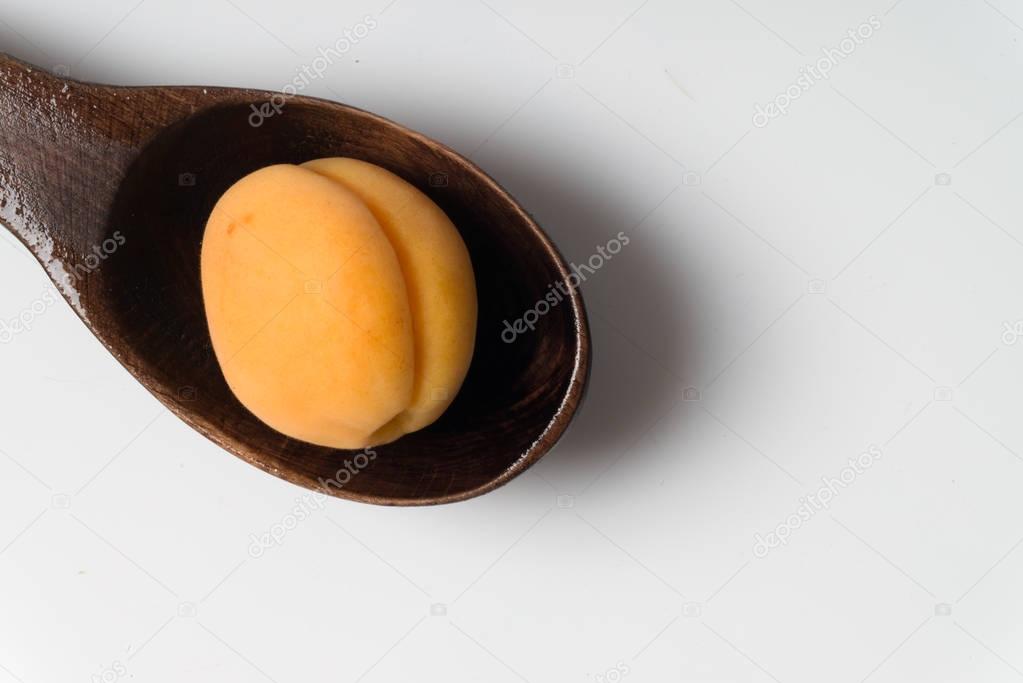Apricot in the wooden spoon with shadow on white background.