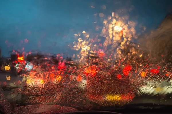 Trafik ışıkları ve şiddetli yağmur sırasında aracın cama araba farlar.