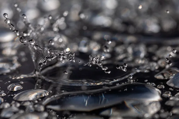 Gotas de agua golpeando contra una superficie negra . — Foto de Stock