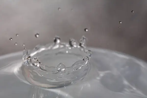 Gotas de agua cayendo sobre la superficie de un vaso lleno de líquido . — Foto de Stock