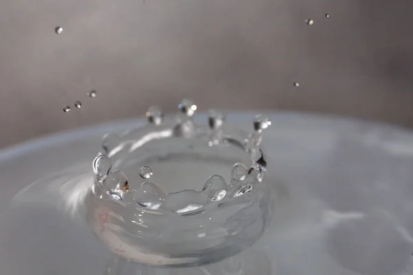 Wassertropfen fallen auf die Oberfläche eines mit Flüssigkeit gefüllten Glases. — Stockfoto