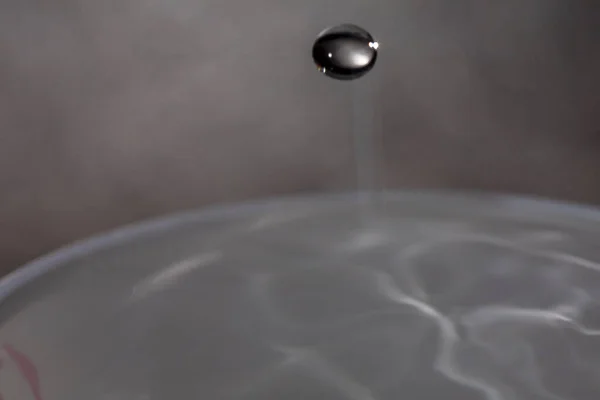 Wassertropfen fallen auf die Oberfläche eines mit Flüssigkeit gefüllten Glases. — Stockfoto