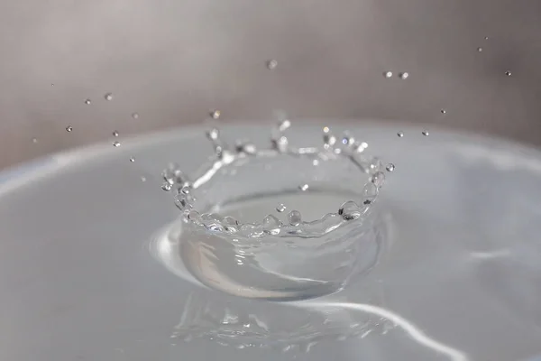 Gotas de agua cayendo sobre la superficie de un vaso lleno de líquido . — Foto de Stock