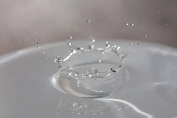 Wassertropfen fallen auf die Oberfläche eines mit Flüssigkeit gefüllten Glases. — Stockfoto